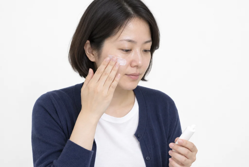 흰 배경에서 30대 여성이 외출 전 볼과 광대에 선크림을 펴 바르는 반신 모습