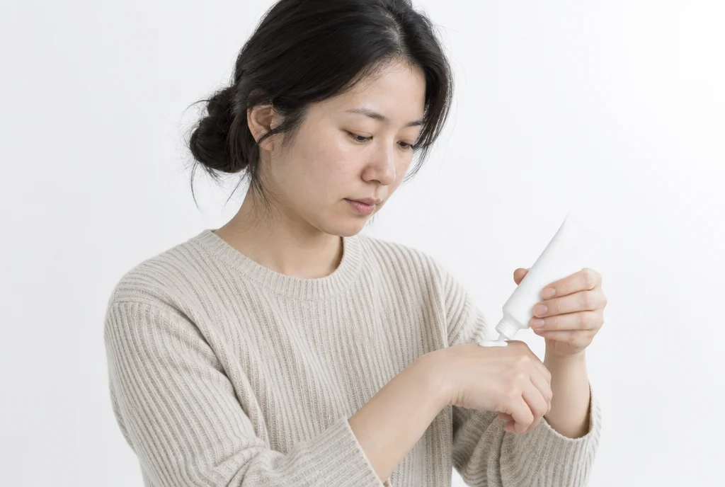흰 배경에서 30대 여성이 손등에 선크림을 덜어 내려다보는 반신 모습